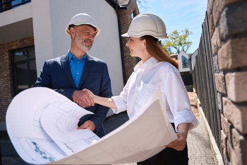 professionals shaking hands at a construction site holding blueprints collaborating on project planning