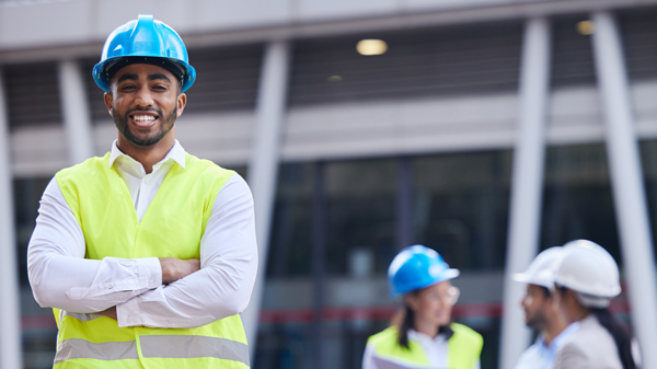 smiling construction worker in safety gear with blue hard hat in foreground with colleagues in background showcasing teamwork and safety measures 1 construction skills