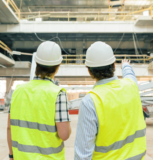 two construction workers discussing building project wearing safety helmets and vests observing construction site progress