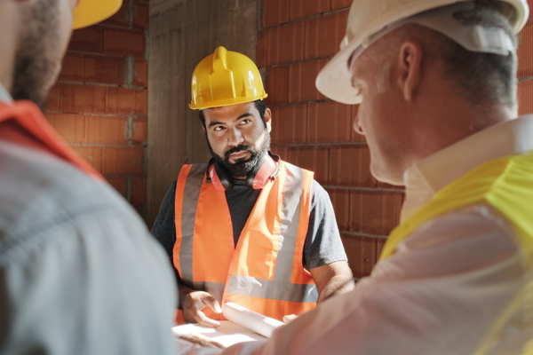 construction workers discussing plans with safety gear in a building site 5 safety guidelines teamwork