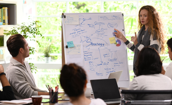 Business meeting with a woman presenting a strategy on a whiteboard while colleagues listen and take notes about collaborative efforts and planning. Effective teamwork approach for successful project development.