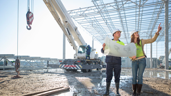 construction site with two workers discussing plans while a crane operates in the background construction project planning collaboration