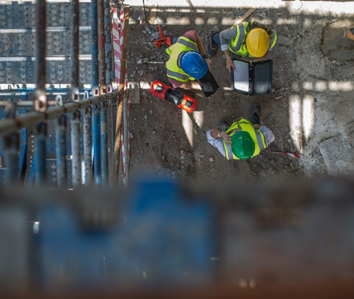 three construction workers discussing plans on site using portable device safety helmets scaffolding background